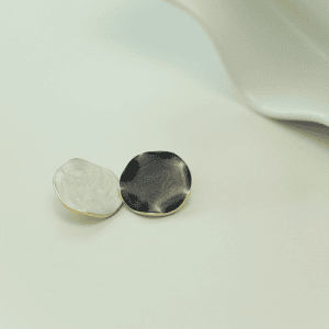 Two minimalist matte shell-pattern round buttons side by side in a light and a dark shade, showing the matte surface