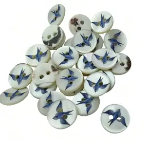 Pile of round shell buttons with two holes, each printed with a blue swallow in flight on a cream pearly face