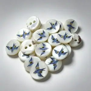 Blue swallow shell buttons on a pale grey background, showing the pearly shell surface and printed bird detail