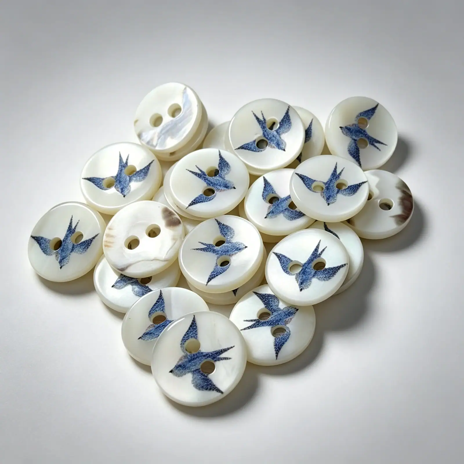 Blue swallow shell buttons on a pale grey background, showing the pearly shell surface and printed bird detail