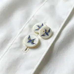 Three blue swallow shell buttons resting on the placket of a white cotton shirt