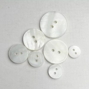 Natural white shell buttons in multiple sizes with a striped 2-hole design in natural shell