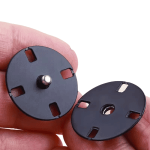 Hand holding a black metal snap button showing the press-stud back and stitching holes, sew-on snap fastener for cardigans and wrap coats
