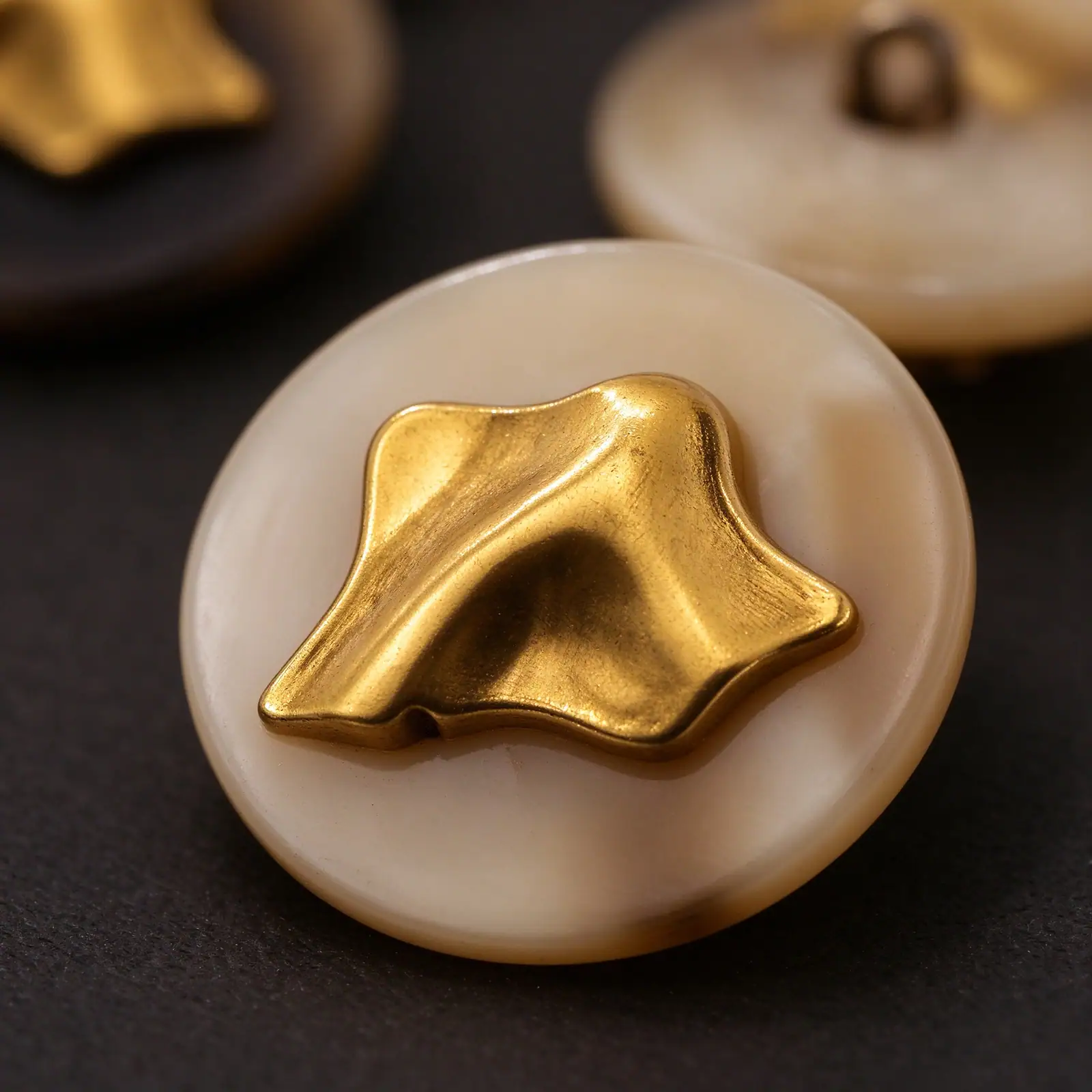 Close-up of a cream horn-look button with a gold-tone metal ornament on top