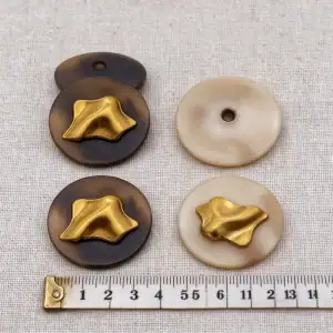 Gold metal buttons in brown and cream next to a centimetre ruler for size