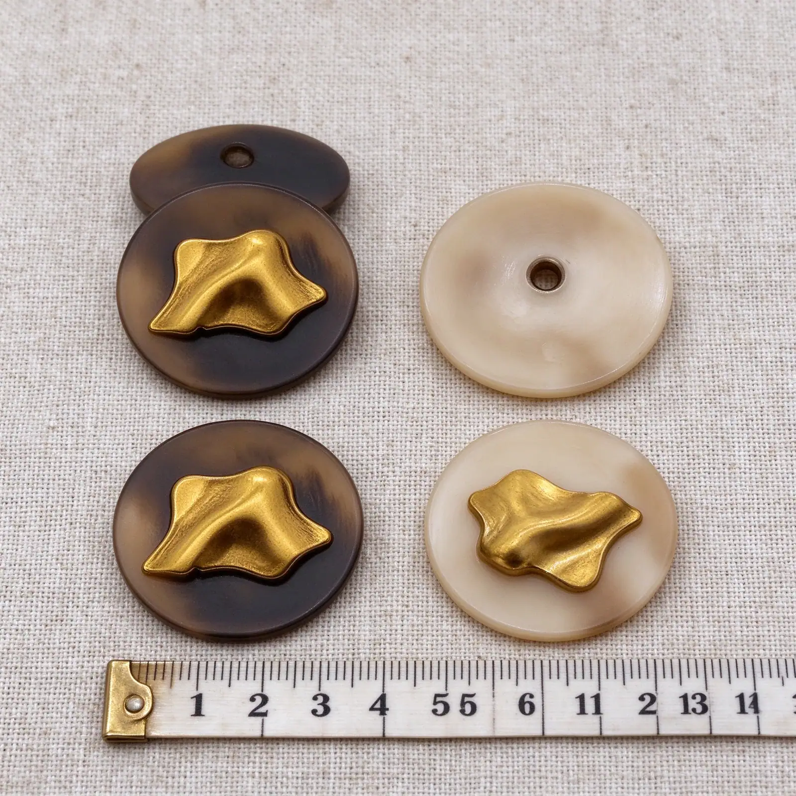 Gold metal buttons in brown and cream next to a centimetre ruler for size