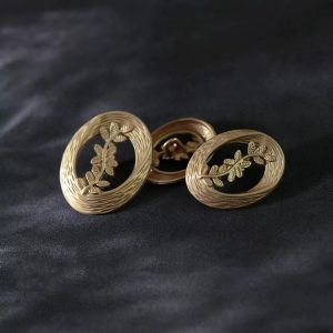 Laurel leaf buttons in vintage gold shown at an angle, openwork oval metal sew-on buttons with woven rims and leaf sprigs