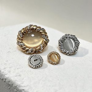 Four rhinestone cat eye buttons in gold-tone and silver-tone on a white stone surface, large and small sizes with champagne and grey cat eye cabochons, one showing the shank back