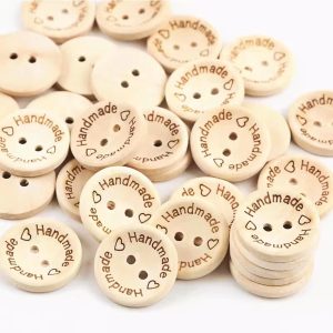 A pile of natural wood two-hole buttons engraved with the word Handmade and small hearts around the rim, shown face up, face down and stacked
