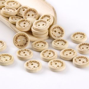 Natural wood two-hole buttons engraved with Handmade with love and hearts, spilling from a wooden tray onto a white surface