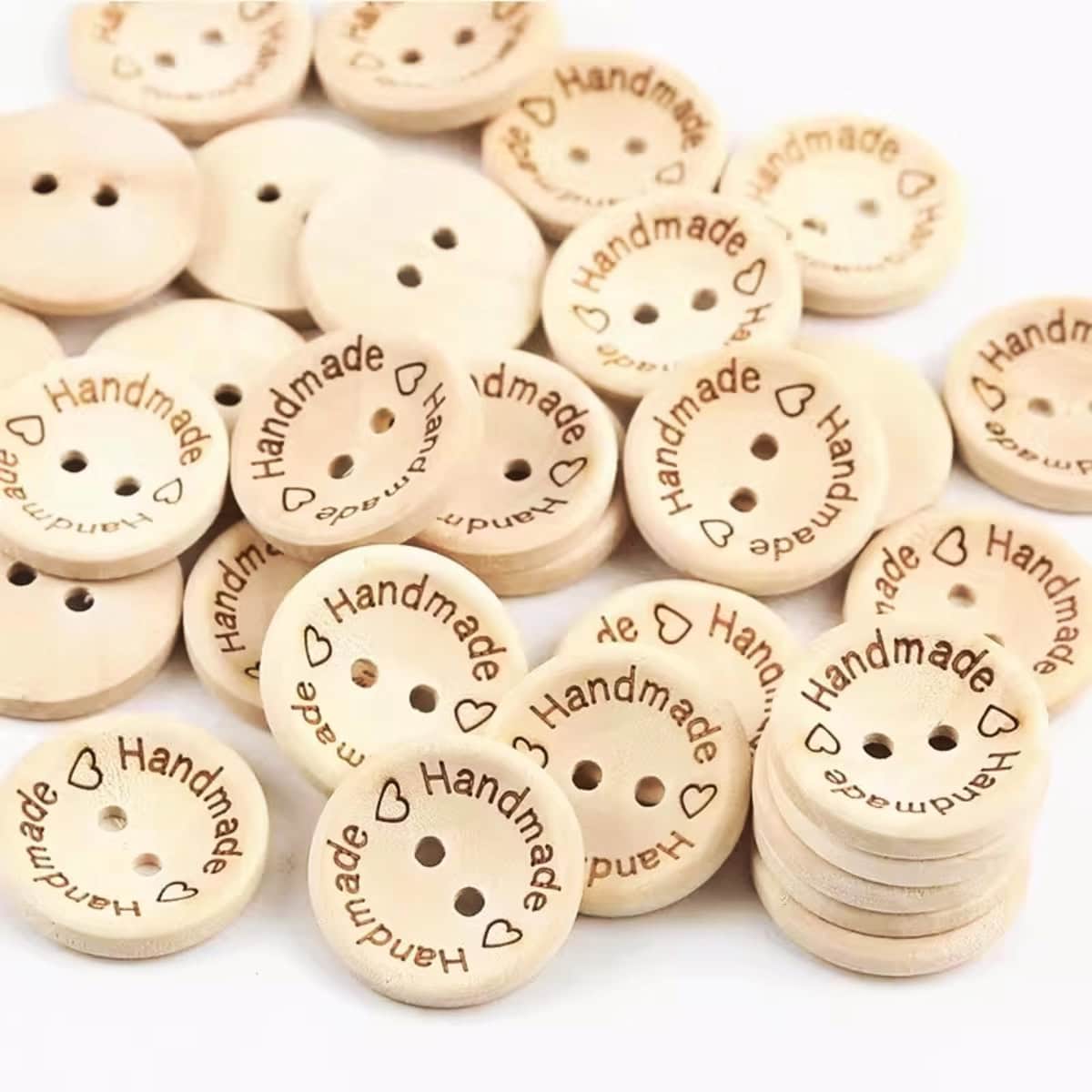 A pile of natural wood two-hole buttons engraved with the word Handmade and small hearts around the rim, shown face up, face down and stacked