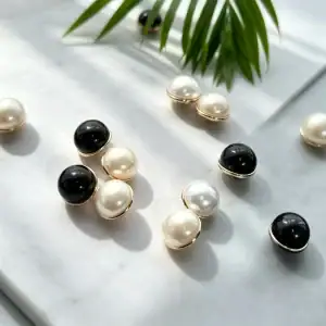 Faux pearl and black mushroom buttons on white marble with a palm leaf