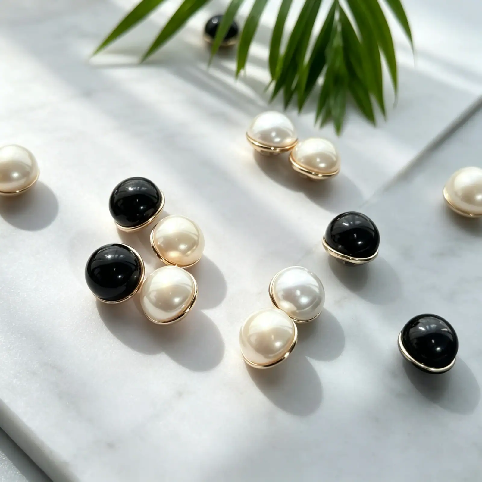Faux pearl and black mushroom buttons on white marble with a palm leaf