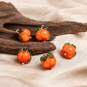 Glass persimmon buttons styled on wood and cloth, handmade orange glass with green tops