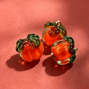 Glass persimmon buttons on a red background, handmade orange glass persimmon shapes with green tops