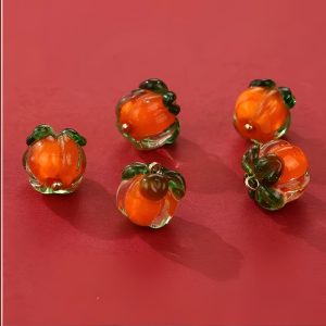 A few glass persimmon buttons on a red background, handmade orange glass with green tops and gold-tone loops