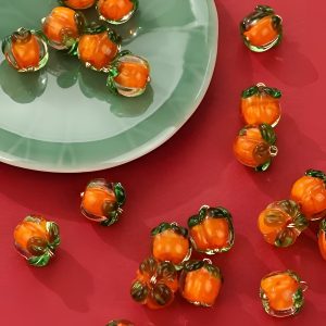 Glass persimmon buttons grouped on a green dish, handmade orange glass with green tops and gold-tone loops