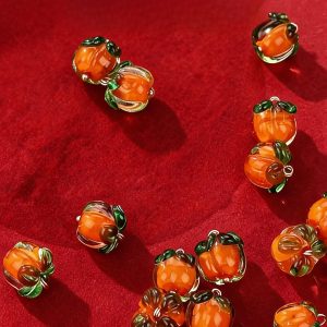 Glass persimmon buttons scattered on a red background, handmade orange glass persimmon shapes