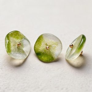 Three green lotus glass buttons with one turned on its side to show the gold-tone loop on the back