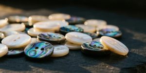 Natural white mother of pearl buttons and iridescent abalone shell buttons scattered on dark slate under raking light