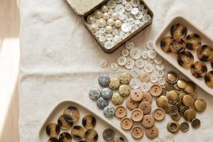 Assorted buttons in faux pearl, gold-tone metal, wood and tortoiseshell resin sorted in trays and a vintage tin for button crafts