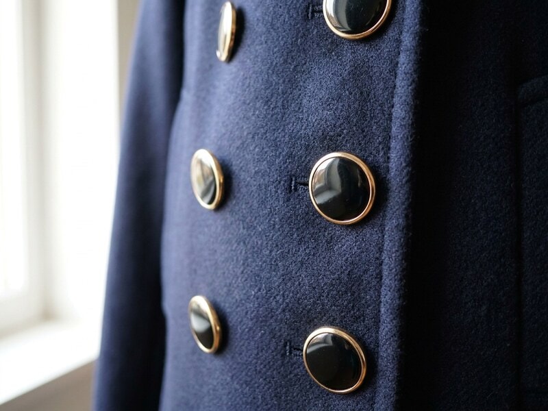 Enamel buttons in black with gold-tone rims sewn in a row down the placket of a navy wool coat