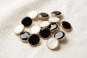 Enamel buttons with glossy black and white faces set in gold-tone metal rims on a linen surface