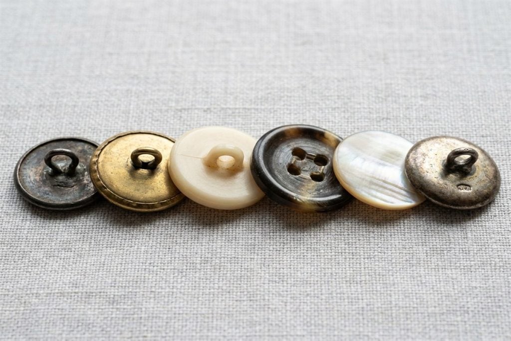 The backs of vintage buttons showing soldered wire loop shanks, a two-piece metal seam and worn sew-through holes