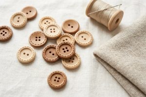 Natural wood buttons with a carved dashed edge in two hole and four hole styles, with a spool of thread and a knit swatch