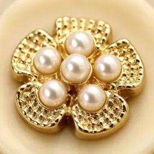 Macro view of a gold-tone flower with six faux pearls set in its centre on a cream resin base