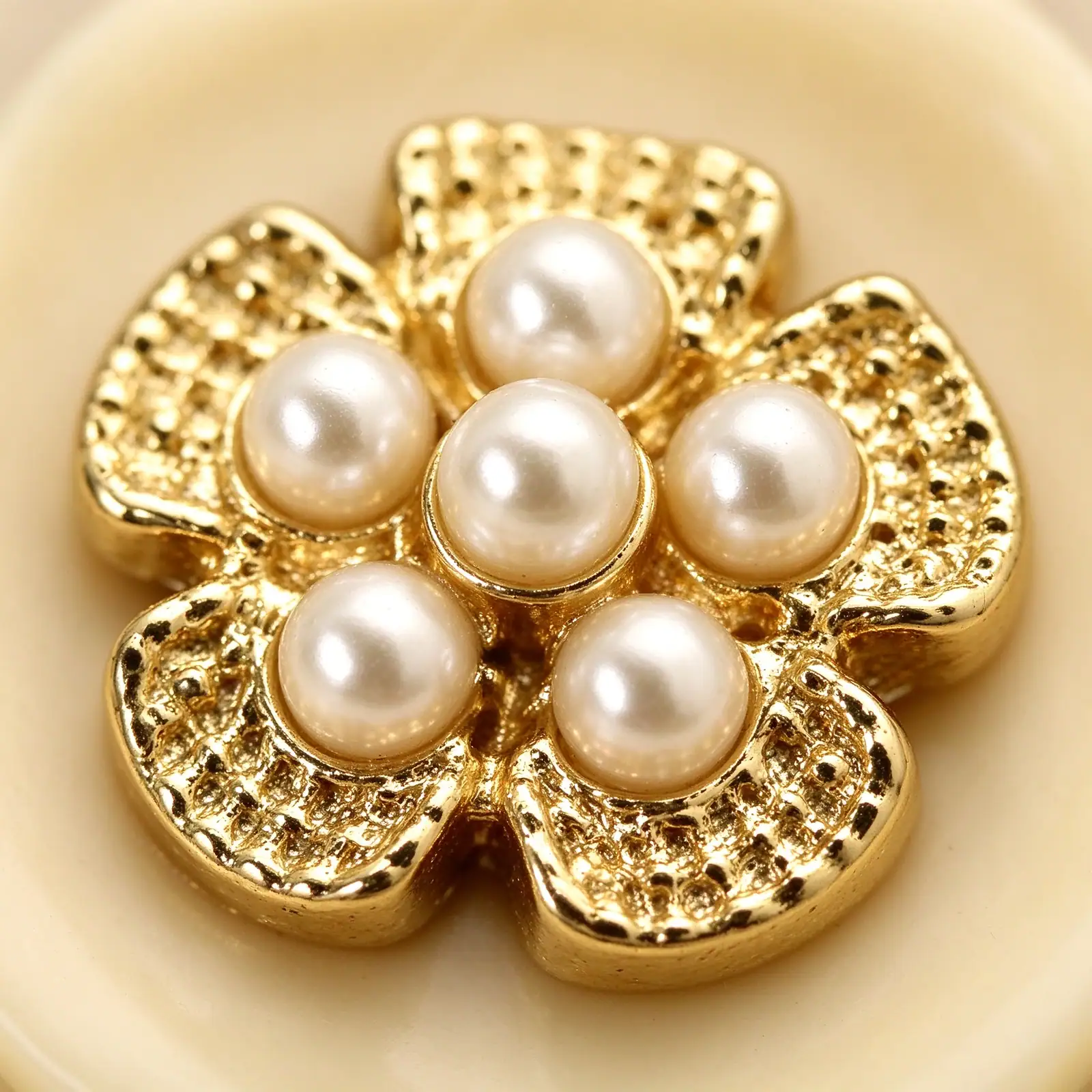 Macro view of a gold-tone flower with six faux pearls set in its centre on a cream resin base
