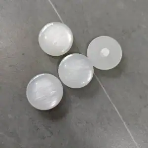 Pearlescent resin buttons on a grey stone surface, one turned to show the shank