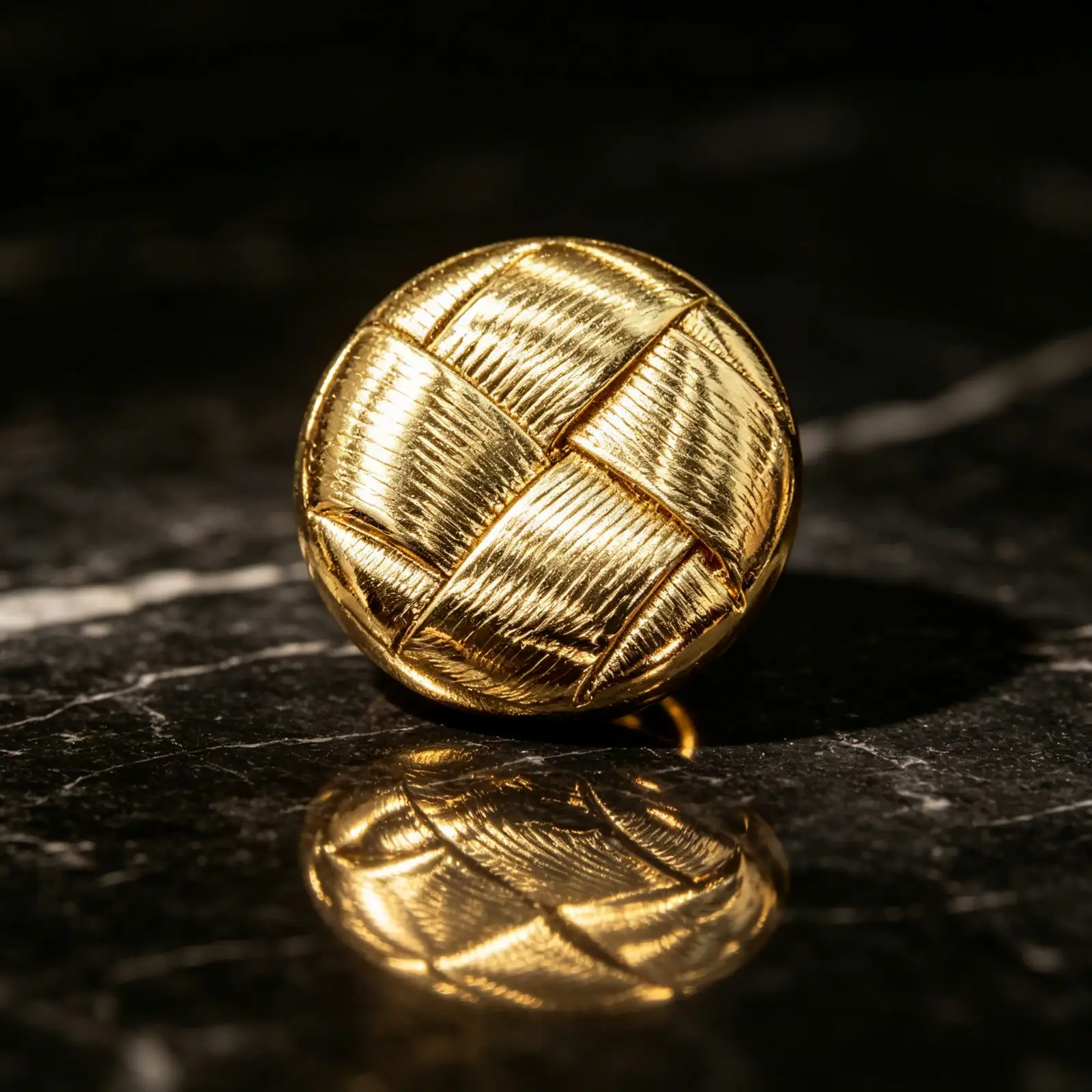 Single round woven gold button on dark marble showing the domed shape and shank back
