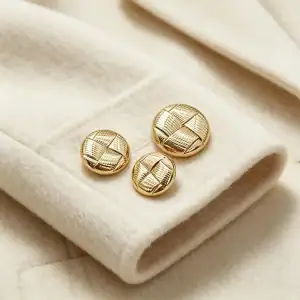 Round woven gold buttons resting on a cream wool coat cuff in three sizes