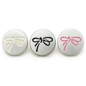 Three silver bow buttons with a matte silver-tone face and a raised ribbon bow outline in cream, black and pink