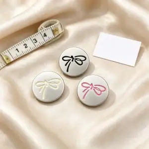 Three silver bow buttons in cream, black and pink on champagne silk beside a tape measure
