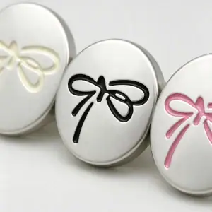 Macro view of three silver bow buttons showing the raised cream, black and pink bow lines on a matte silver face