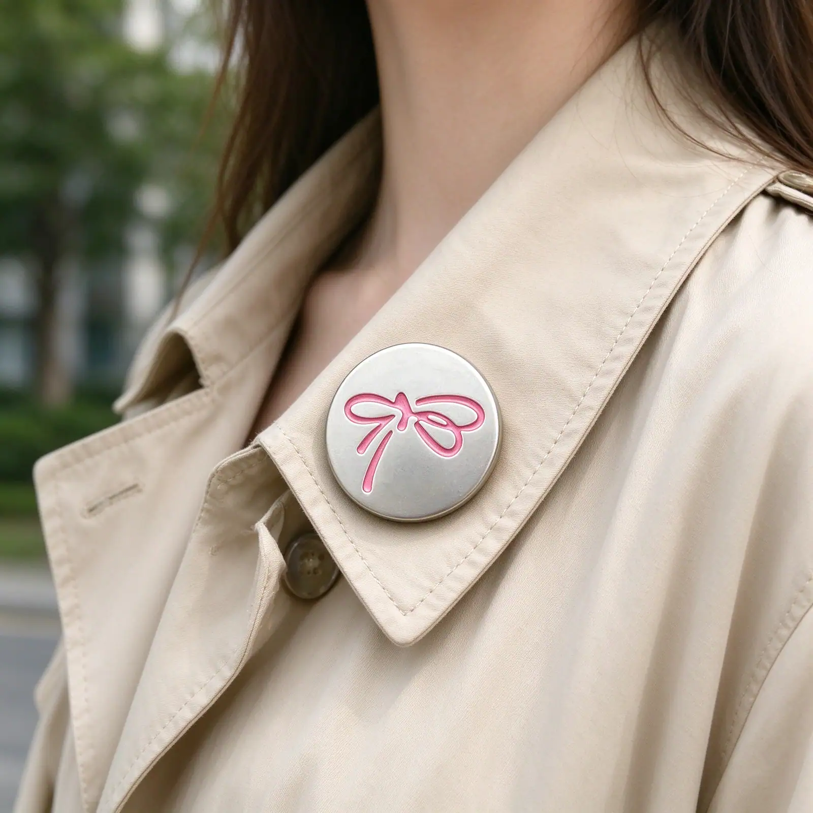 Silver bow button with a pink ribbon bow on the lapel of a beige trench coat