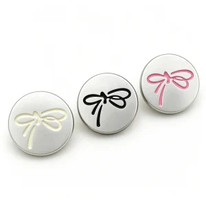 Silver bow buttons in cream, black and pink arranged in a diagonal row on a white background