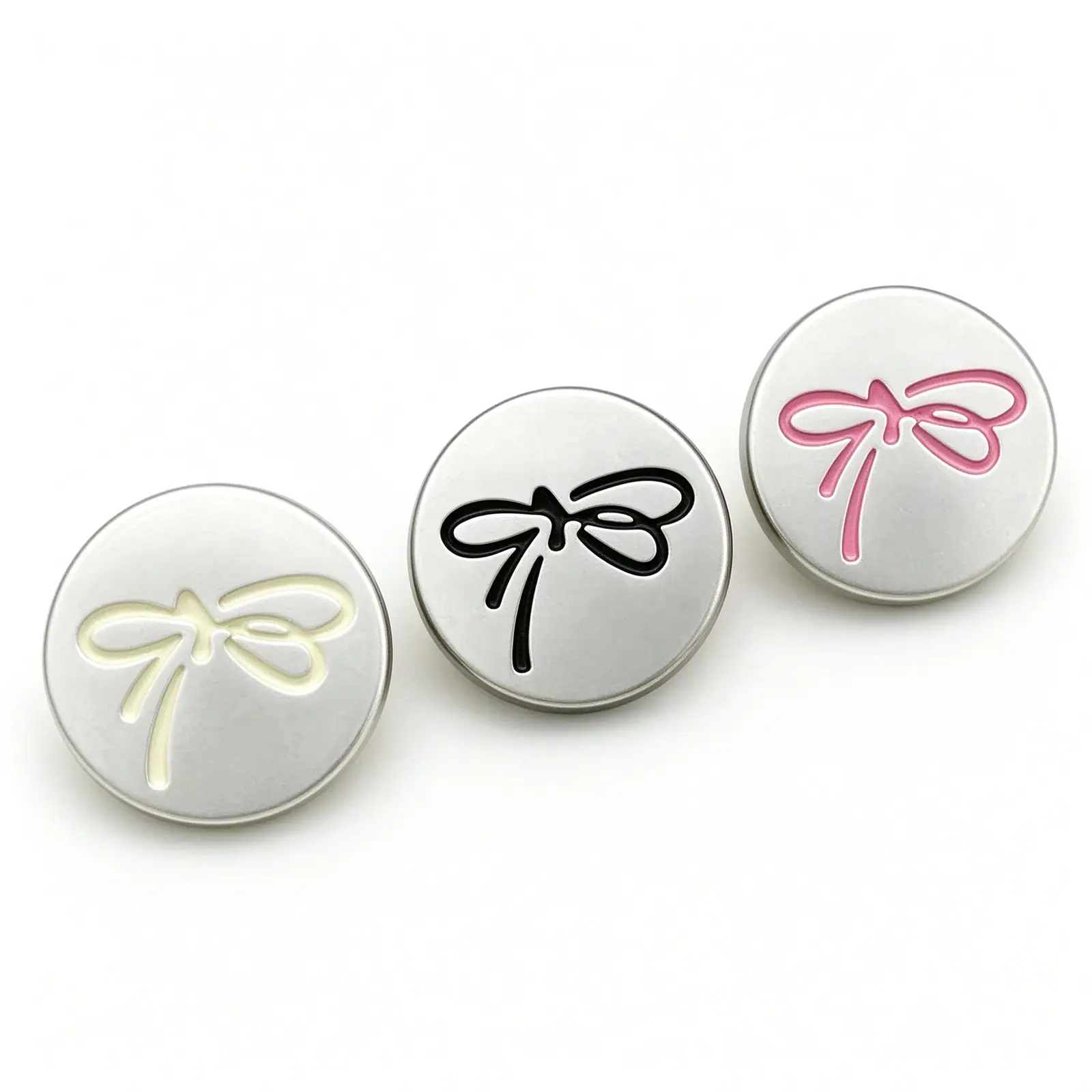 Silver bow buttons in cream, black and pink arranged in a diagonal row on a white background