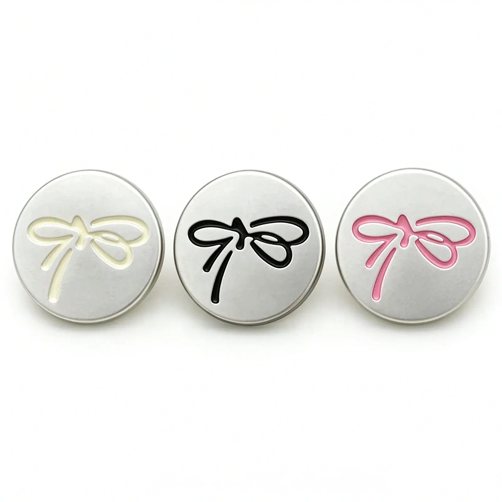 Three silver bow buttons with a matte silver-tone face and a raised ribbon bow outline in cream, black and pink
