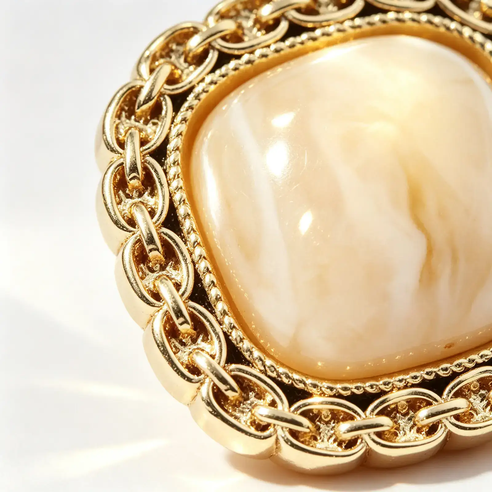 Close up of a cream square chain link button showing the gold-tone chain-link rim, twisted rope inner ring and glossy marble-look resin dome