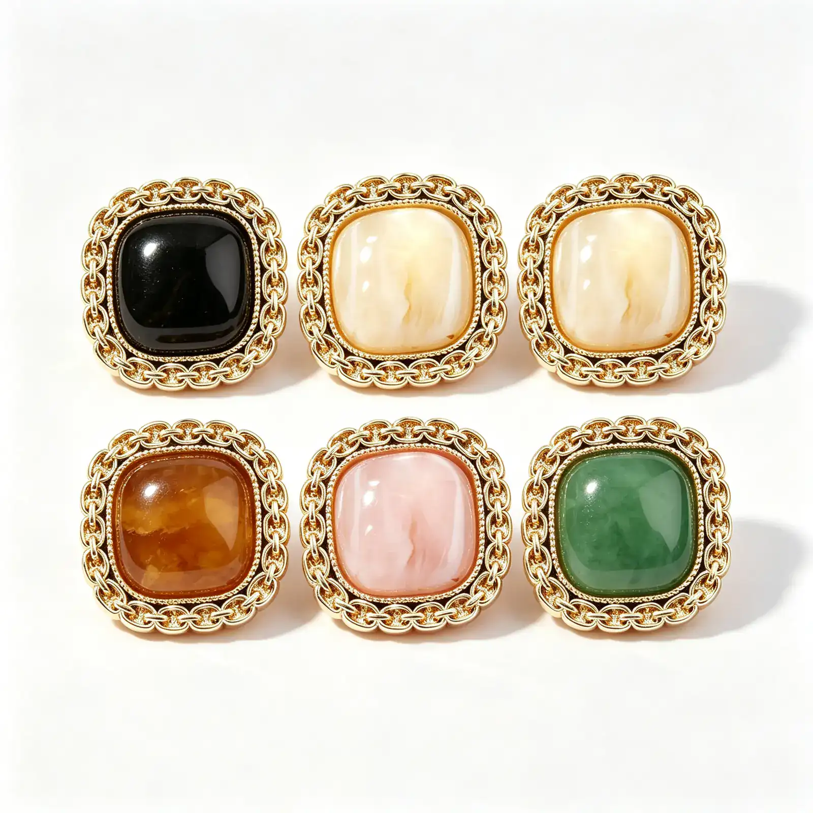 Six square chain link buttons in black, cream, brown, pink and green, each with a gold-tone chain-link rim around a domed marble-look resin face