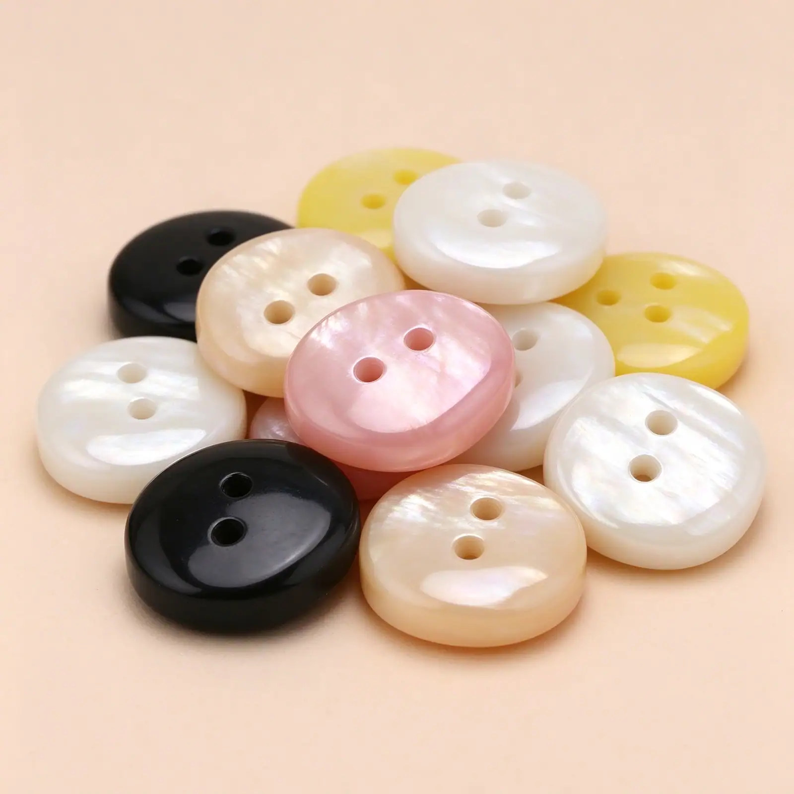A pile of square resin buttons in black, white, cream, pink and yellow showing the pearl-look streaking on each