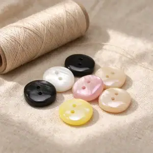 Resin buttons in black, white, pink, yellow and cream laid on linen fabric next to a spool of thread