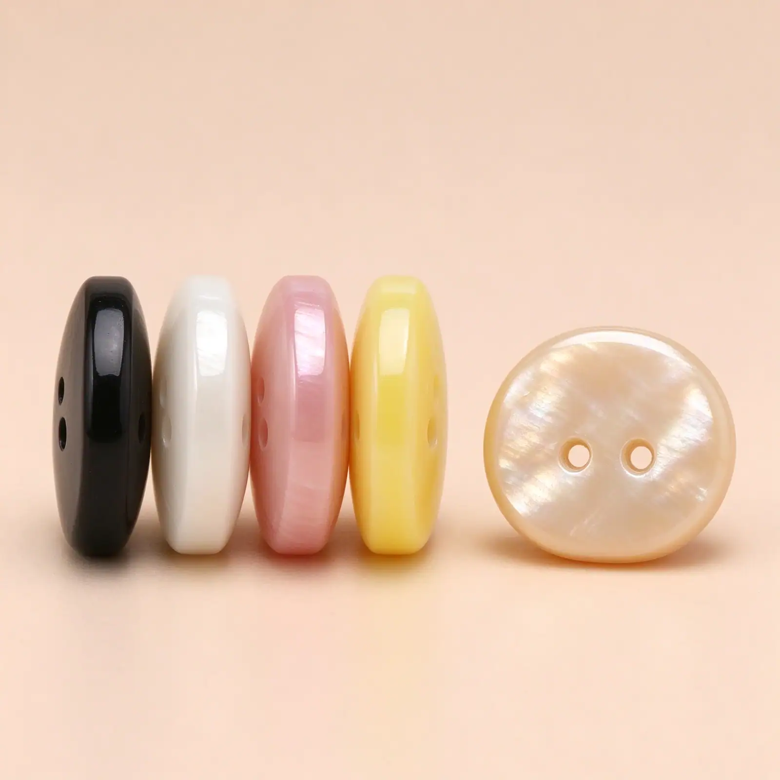 Four resin buttons standing on edge showing their thickness, with a cream button lying face up beside them